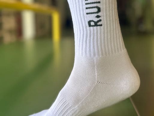 Witte R.UIT anti-slipsokken aan een voet, met de sportvloer op de achtergrond